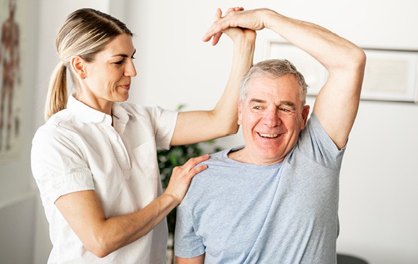 A female physical therapist helps a senior stretch his tricep
