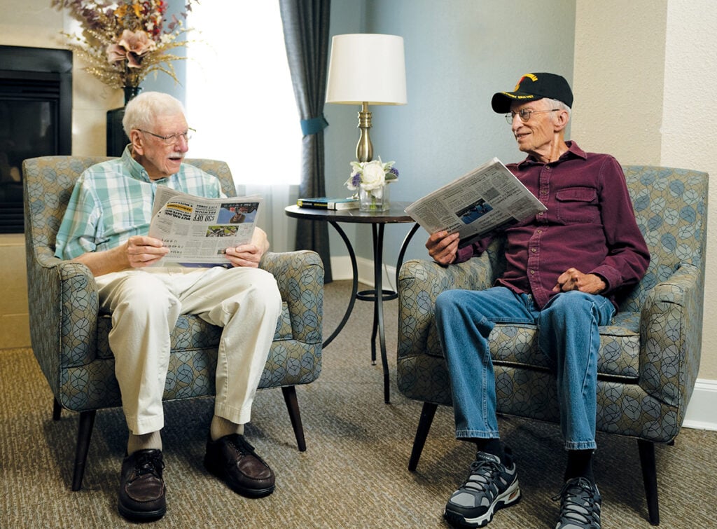 Two older adult men read the newspaper together at their senior living community