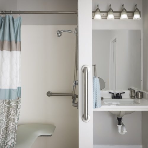 Senior living apartment bathroom with a sink, mirror and walk-in shower that includes a shower bench