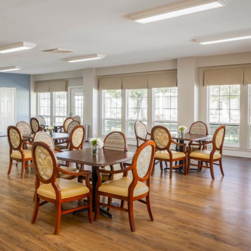 Large open room with multiple tables and chairs along with a piano and many windows