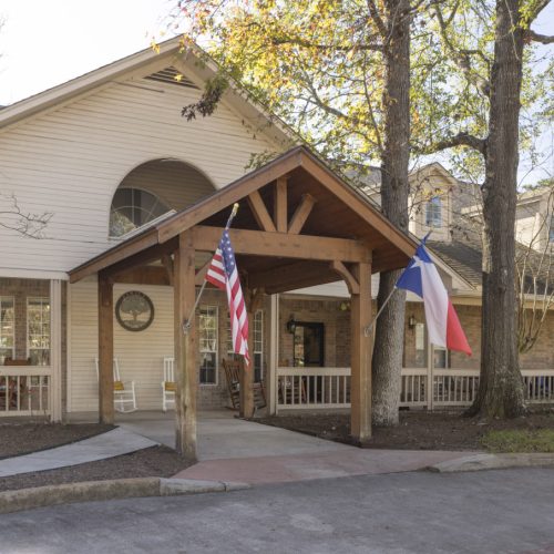 Front entrance with brick facade and trees to Wellington at Conroe senior living community in Conroe, Texas