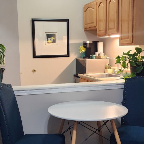 Apartment kitchen in a senior living community includes a microwave, sink, mini fridge, storage and a small table and chairs