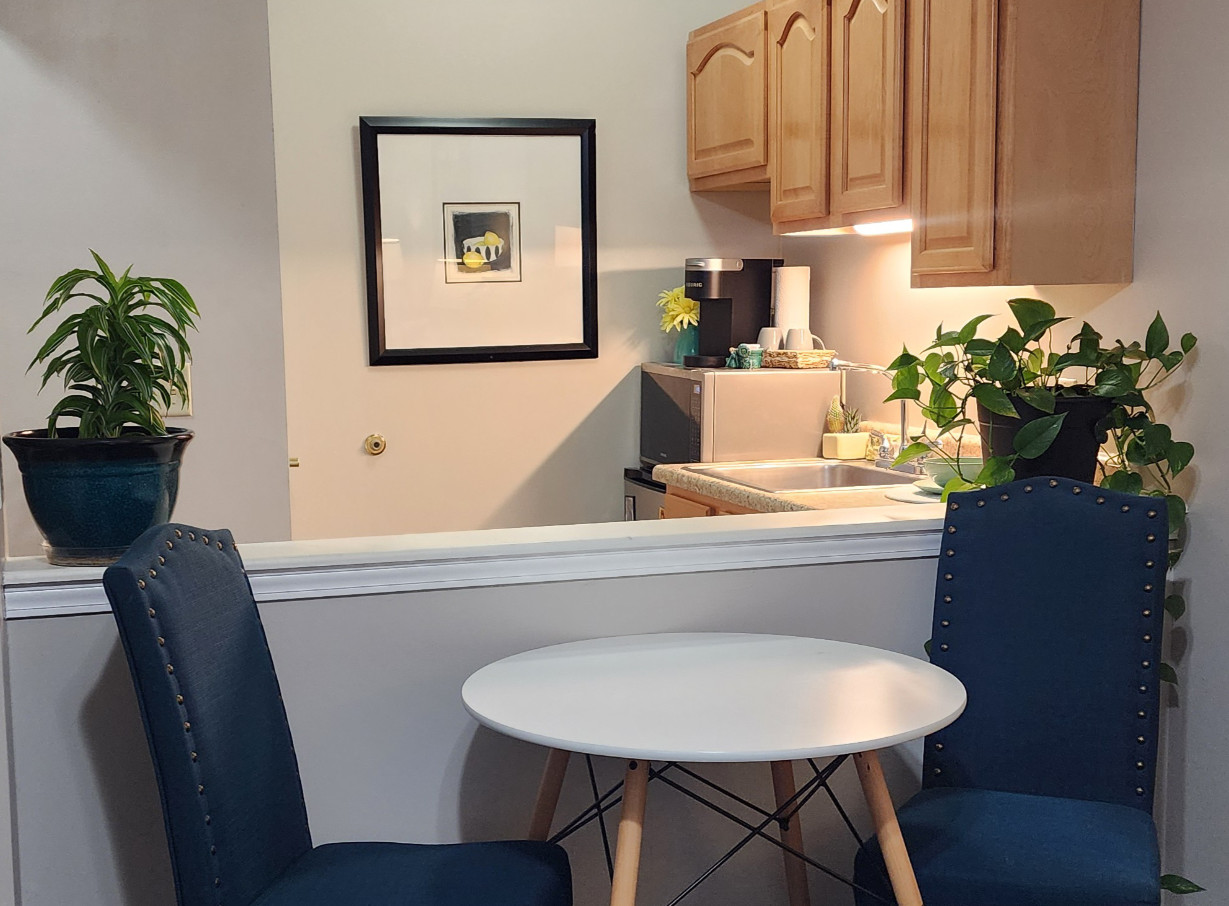 Apartment kitchen in a senior living community includes a microwave, sink, mini fridge, storage and a small table and chairs