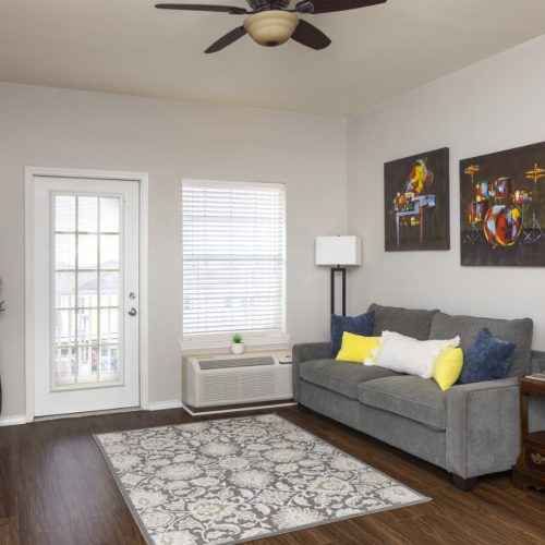 Apartment living room includes a couch, side tables, window, balcony and TV