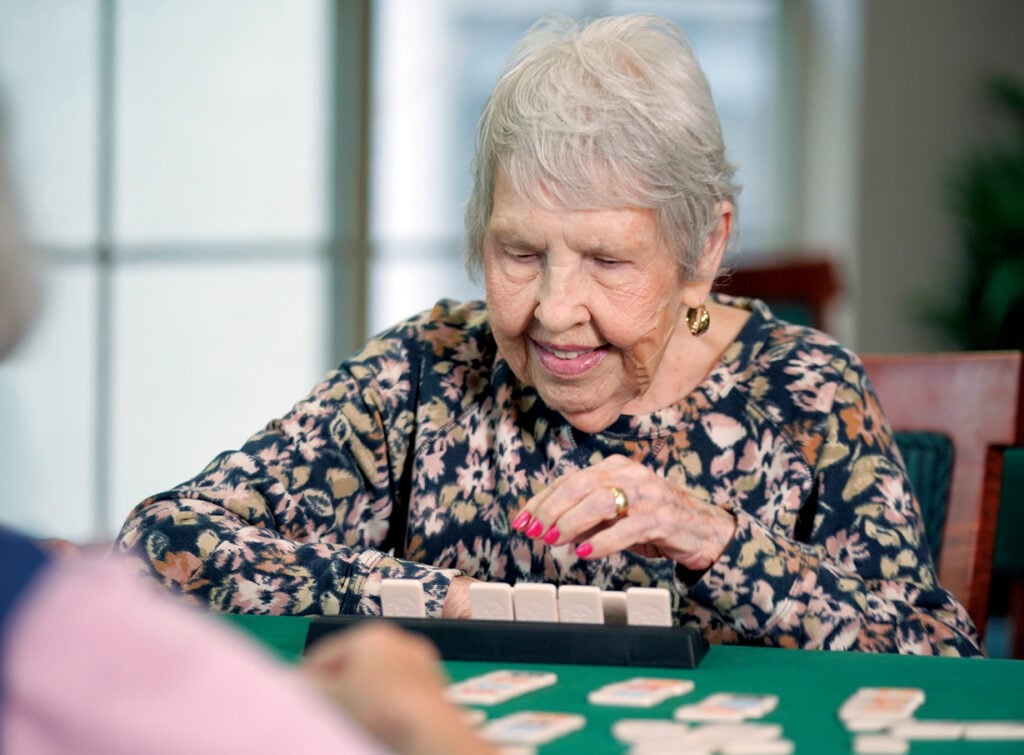 Older woman smiles while playing dominoes at her senior living community