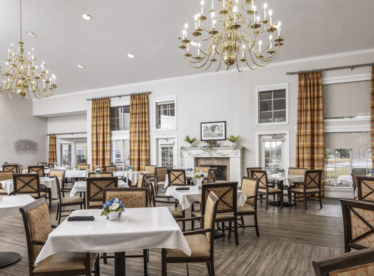 A large and elegant dining room with plenty of seating, a fireplace, large windows and chandeliers in San Antonio, Texas