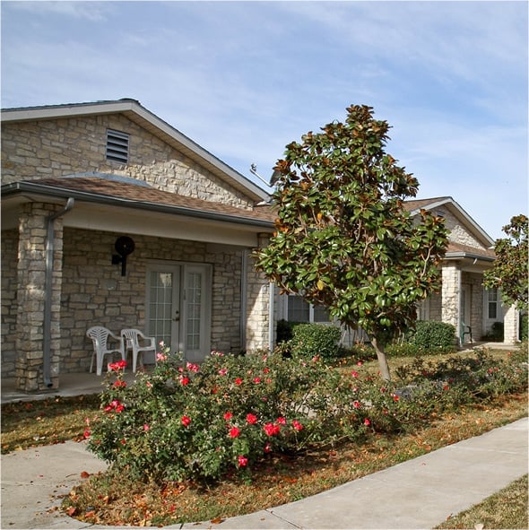 Outdoor patios with rocking chairs surround a beautifully landscaped courtyard with a walking path in Stephenville, Texas..