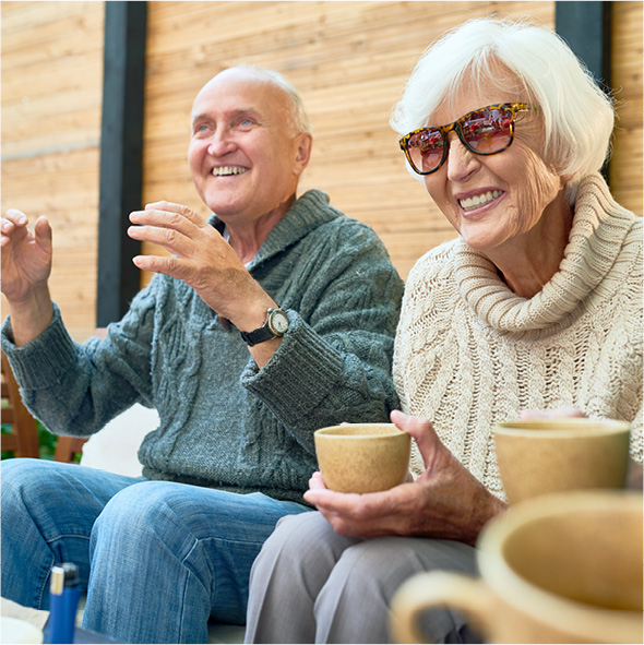 Happy seniors enjoying coffee outdoors in sweaters and sunglasses.