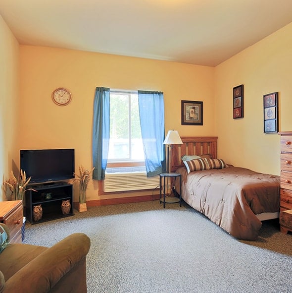Model apartment with a bed, TV and comfortable chair in a spacious living/sleeping area in Park Falls, Wisconsin.
