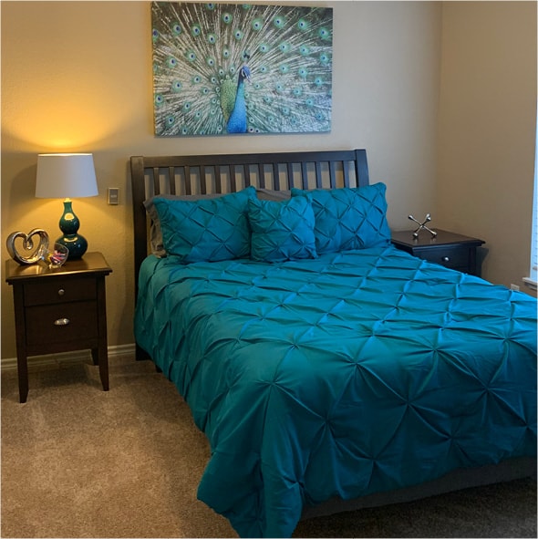 A model apartment with peacock artwork, bright blue bedding and a lamp and nightstand in Irving, Texas.