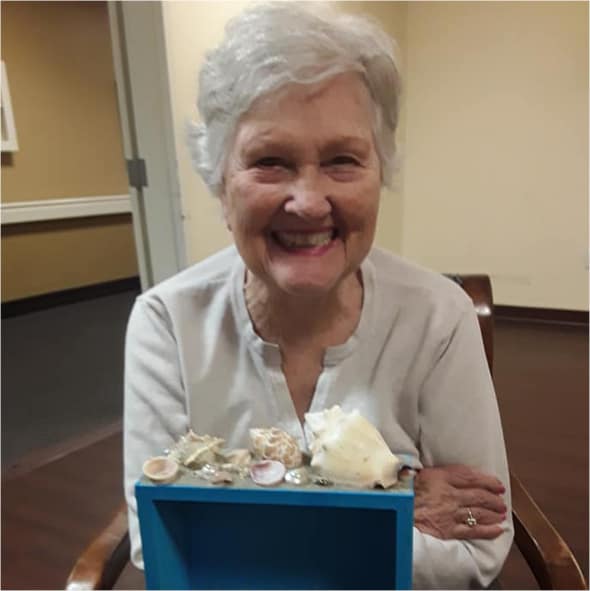 A smiling resident showing off her completed shadow box made with sea shells in Virginia Beach, Virginia.