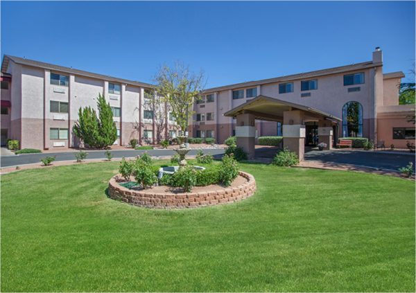 Three-story, stucco building in 2 colors with a portico entrance, benches, fountain and landscaping in Cottonwood, Arizona.
