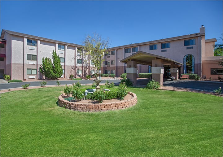 Three-story, stucco building in 2 colors with a portico entrance, benches, fountain and landscaping in Cottonwood, Arizona.