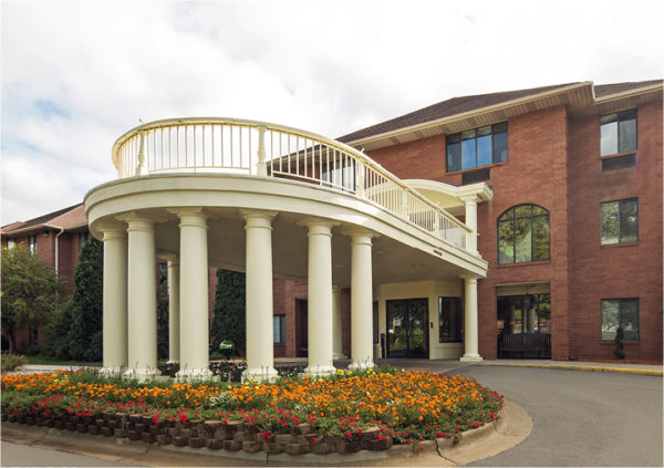 A brick senior living community with a porch and beautiful flowers in East Lansing, Michigan.