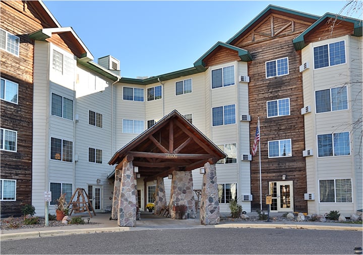 Exterior of senior living community with wood and white siding and a portico with stone pillars in Maple Grove, Minnesota.