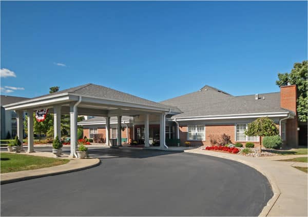 Front entrance of a senior living facility in Williamsville, New York with covered circular drive and lush landscaping.