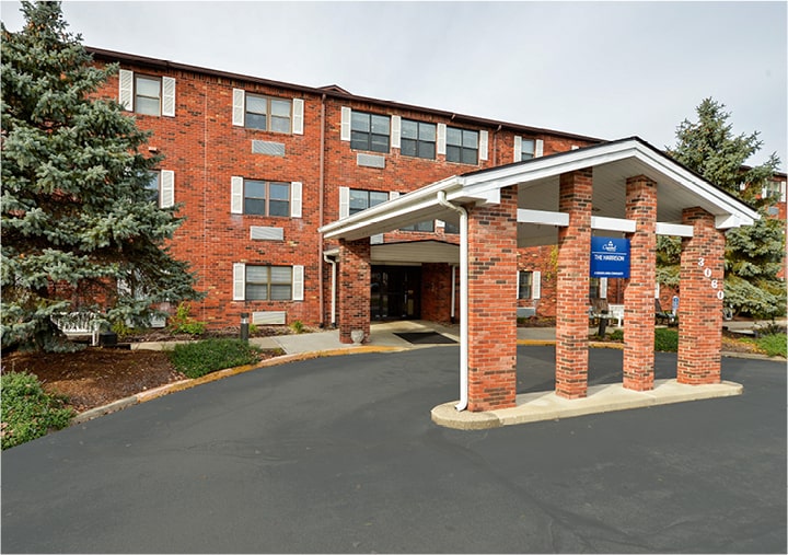 Multi-story brick building with portico drive-thru entrance, columns and large pine trees in Indianapolis, Indiana.