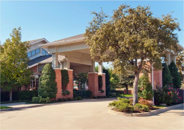 The outside of an independent living community in Irving, Texas with mature trees and lush grounds.