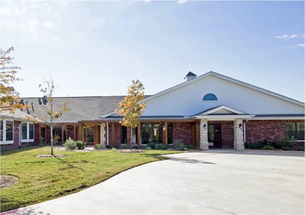 Front entrance of a brick senior living facility with green grass and trees in College Station, Texas.
