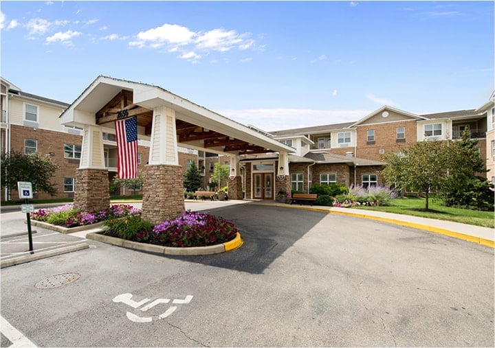Front entrance of a senior living facility in Dayton, Ohio with lush landscaping and covered driveway.