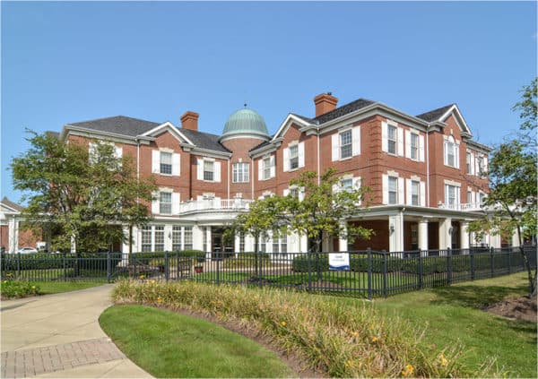 Front entrance of a senior living facility in Shaker Heights, Ohio with lush landscaping and a wrought iron fence.