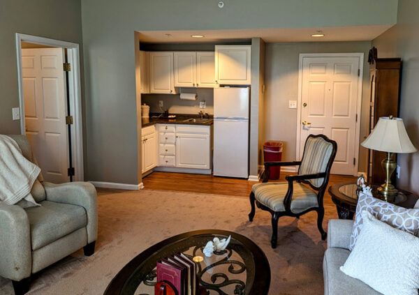 Senior living apartment living room with a couch, chairs and kitchenette that includes a fridge, sink and cabinets in Greencastle, IN