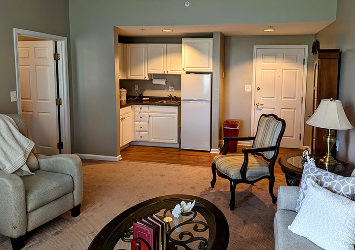 Senior living apartment living room with a couch, chairs and kitchenette that includes a fridge, sink and cabinets in Greencastle, IN