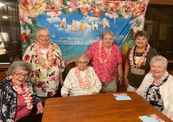 Six senior women smile while at a Hawaiian-themed party at their senior living community in Greencastle, Indiana