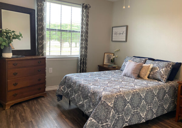 Apartment bedroom with a bed, dresser and two nightstands at a senior living community in Lake Granbury, Texas.