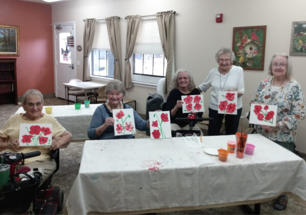 Five senior women smile while holding their paintings in Lake Granbury, Texas.