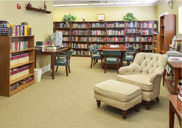 A large library with surrounding walls filled with bookshelves and a comfortable lounge chair among tables in Mesquite, Texas..