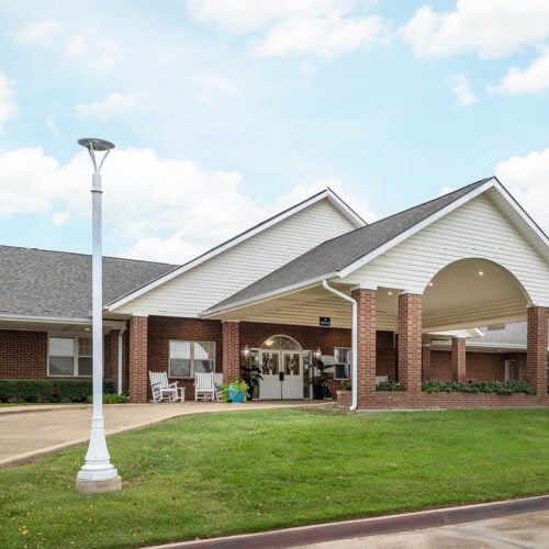 Whitley Place - Senior living in Keller, Texas. Front entrance of a senior living facility in Keller, Texas with covered walkway and white rocking chairs.