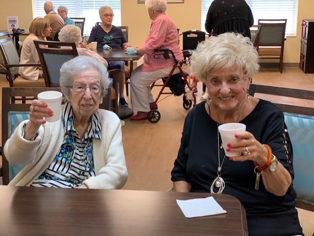 Two senior ladies smiling with their drinks at senior living facility in Williamsville, New York.