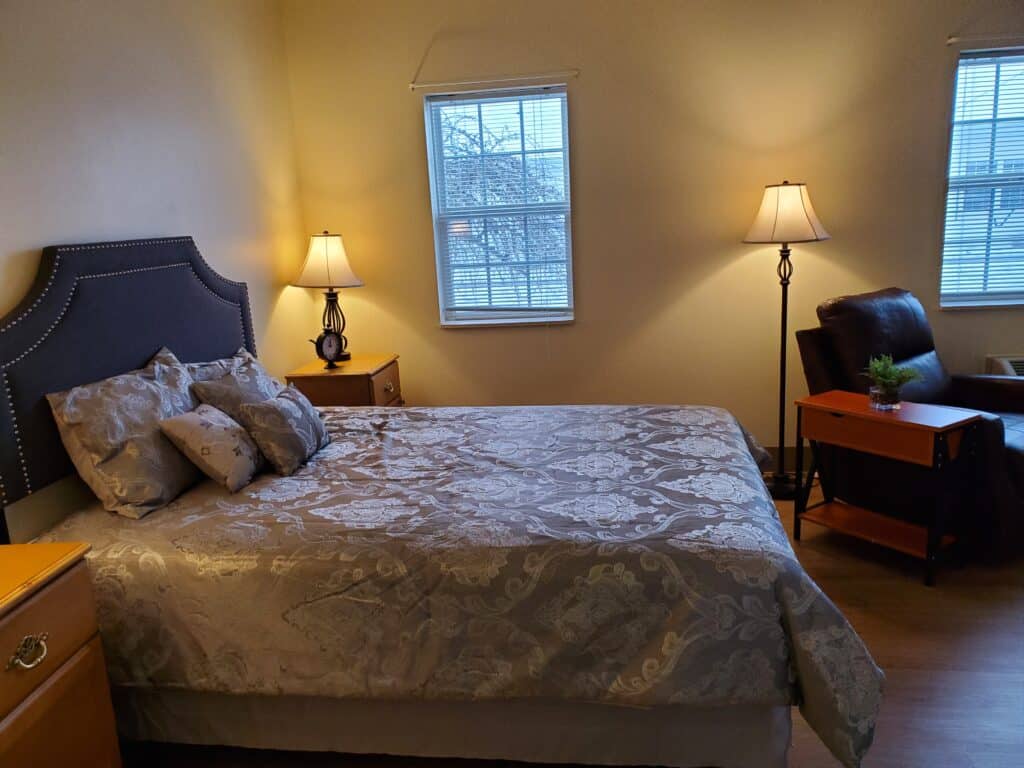 Model apartment bedroom with full size bed and recliner at senior living facility in Chardon, Ohio.