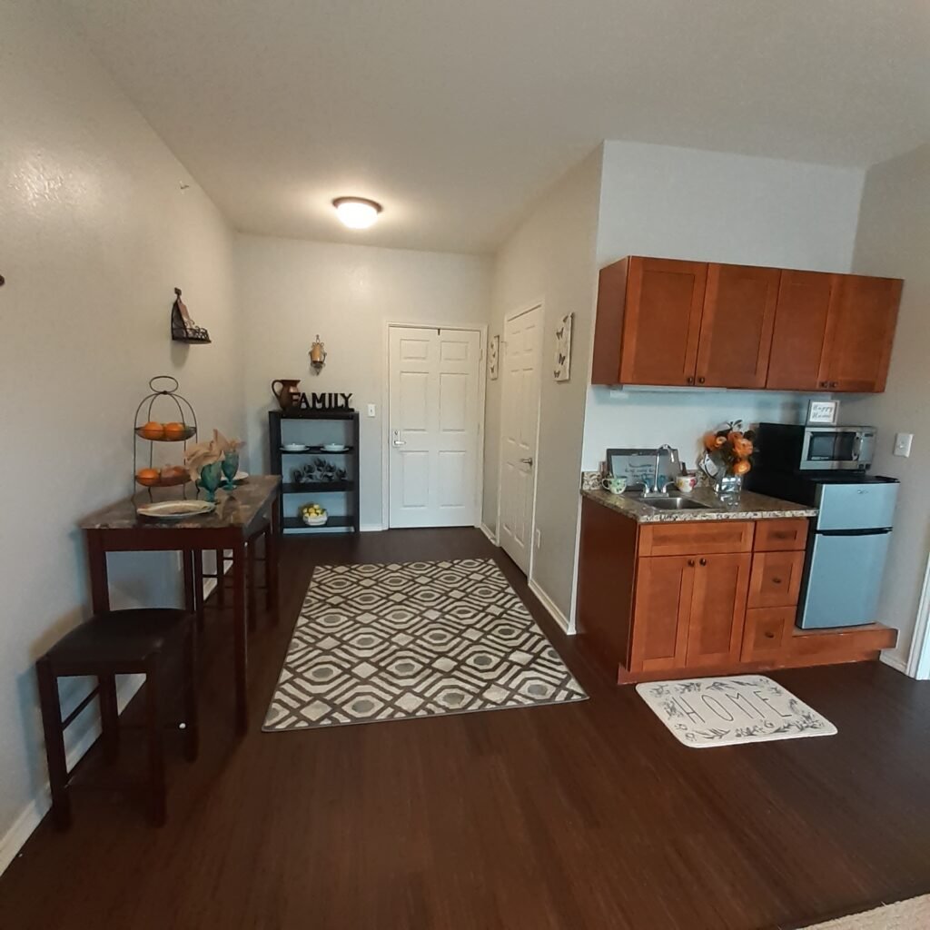 Dining room and kitchenette with refrigerator and within an apartment at a senior living community in San Antonio, Texas.