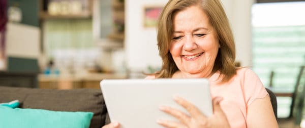 A smiling woman reading a blog on her tablet.