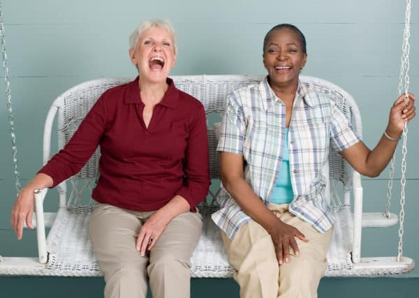 Two friends laughing and swinging on a porch swing.