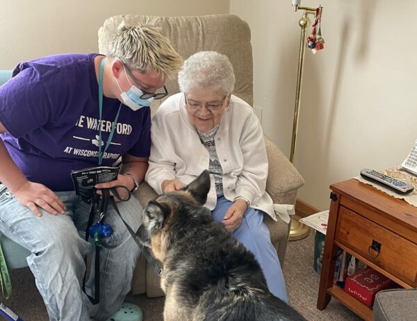 senior woman and caregiver smile and pet a therapy dog