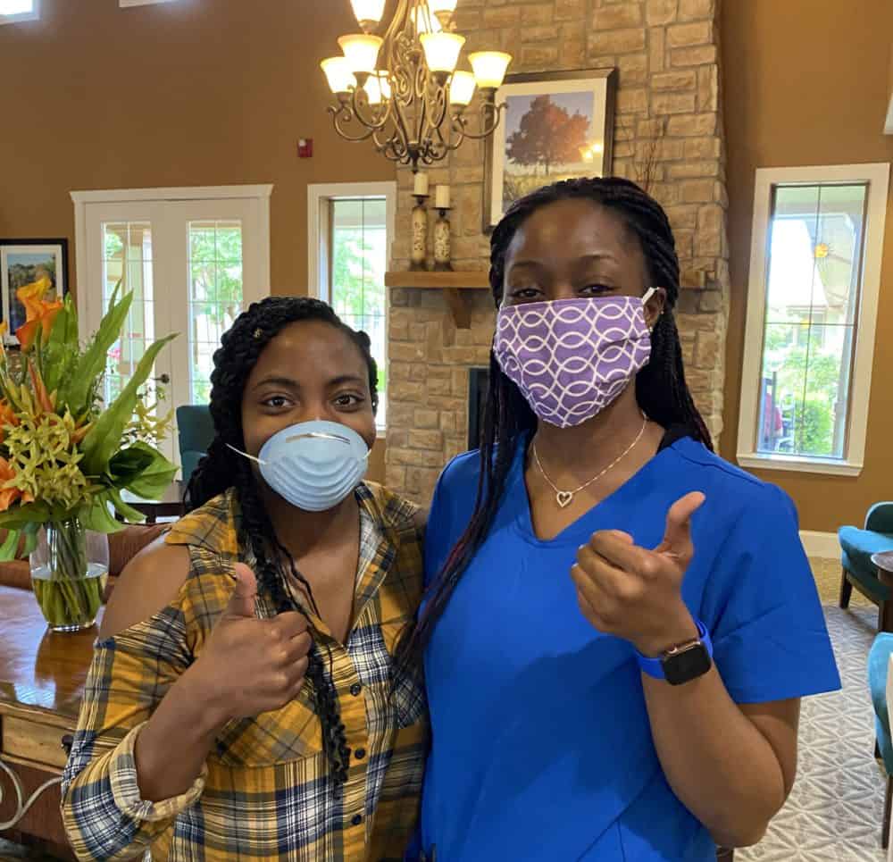 Two-women-caregivers-give-thumbs-up-in-senior-living-facility.