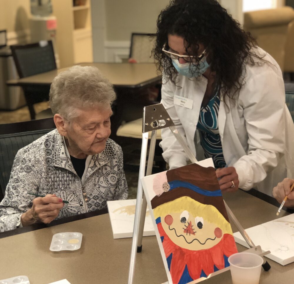 An employee assists a senior woman with a painting project at a senior living community in Fort Wayne, Indiana.