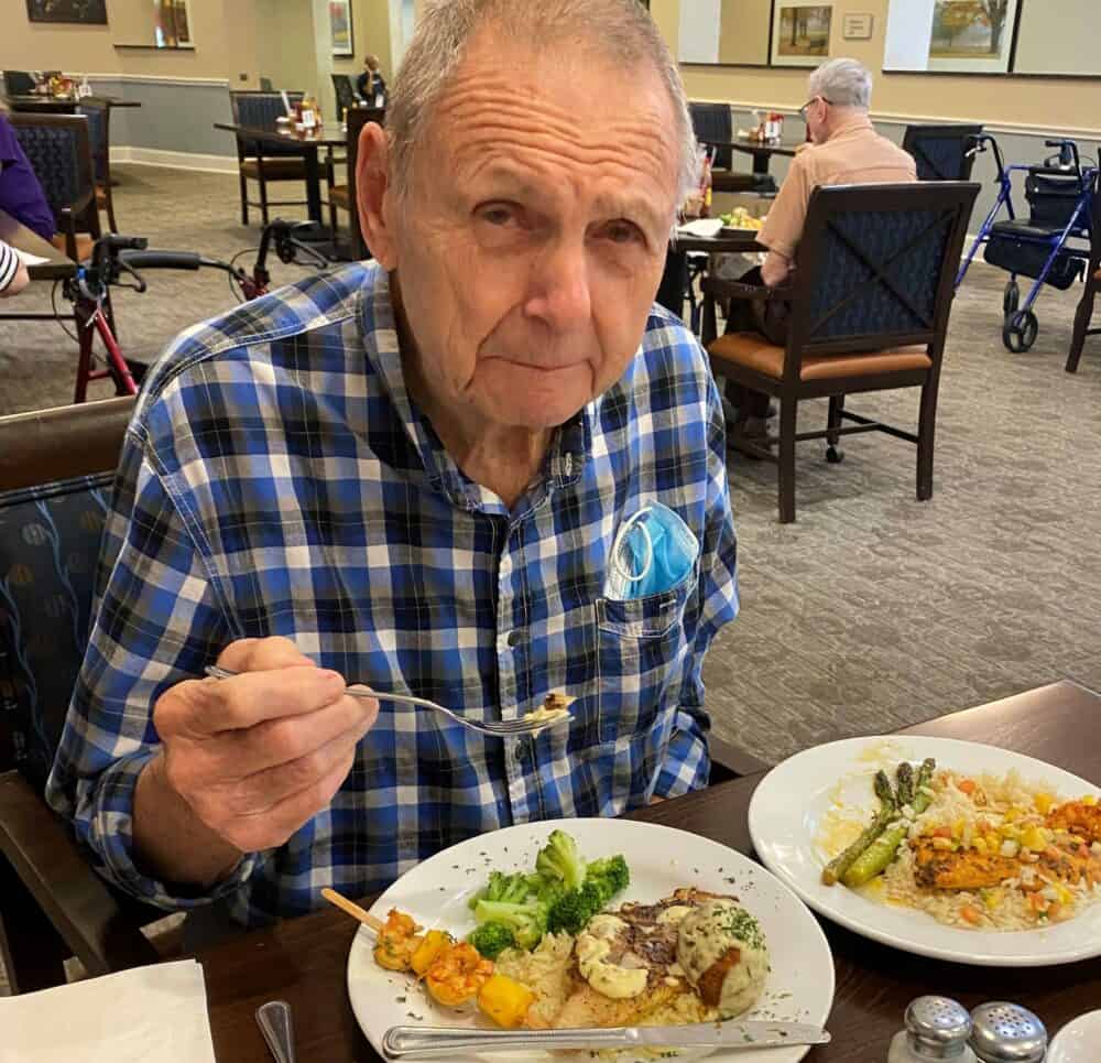 Senior man smiles with a mouthful of food at a senior living facility in Richardson, Texas.