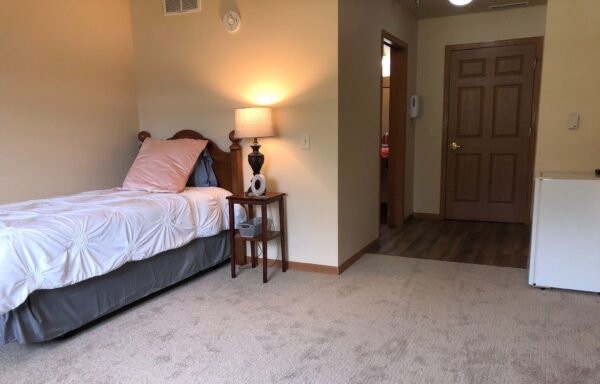 A senior apartment model bedroom with bed and nightstand at senior living community in Plymouth, Wisconsin.