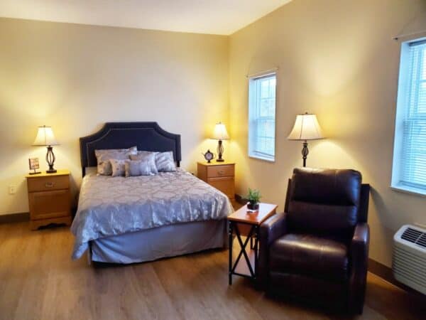 Senior apartment bedroom with bed, chair and nightstands at a senior living community in Chardon, Ohio.
