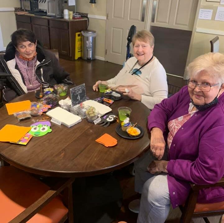 three senior women smile while enjoying a Halloween party
