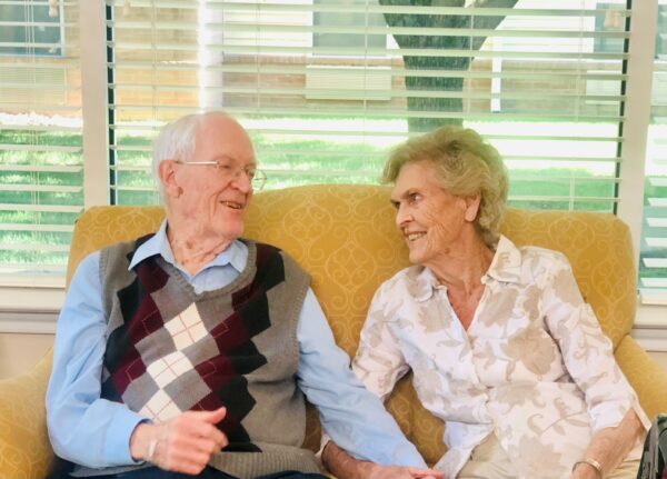 Senior man and woman smile at each other on the couch at a senior living community in Springfield, Missouri.