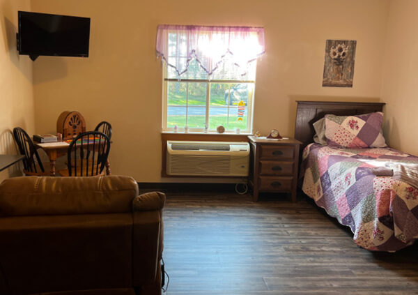 studio apartment with a twin bed near a window, a TV, seating area and a lounge chair