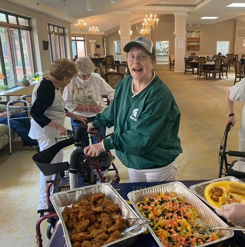 Senior woman smiles while getting food for the football party at a senior living community in East Lansing, Michigan.