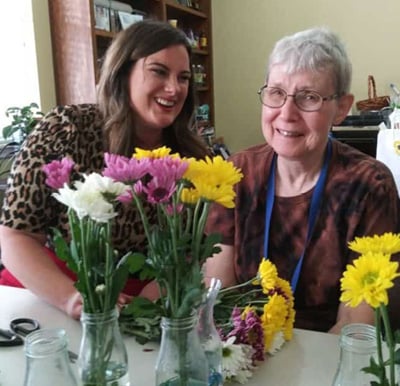 Two older women smiling with some yellow and pink flowers at Whitley Place in Keller, Texas.