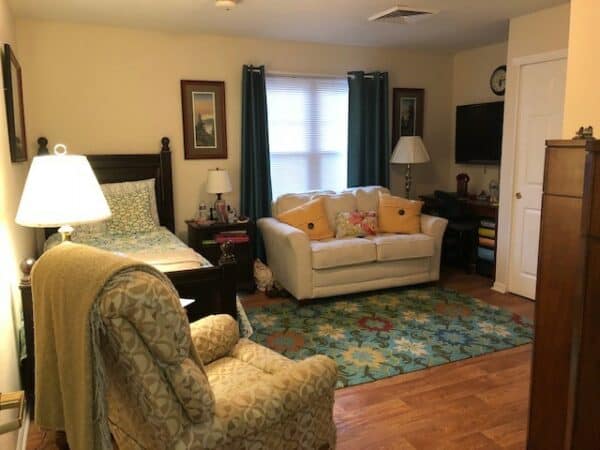 Studio apartment with bed, couch, chair and television at a senior living community in Jeffersonville, Indiana.