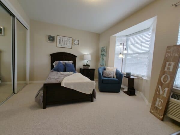 Bedroom in a senior apartment with bed, nightstand and chair at the Waterford at Baytown, located in Baytown, Texas.